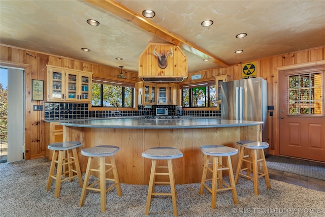 kitchen with a breakfast bar, light carpet, stainless steel refrigerator, and wooden walls