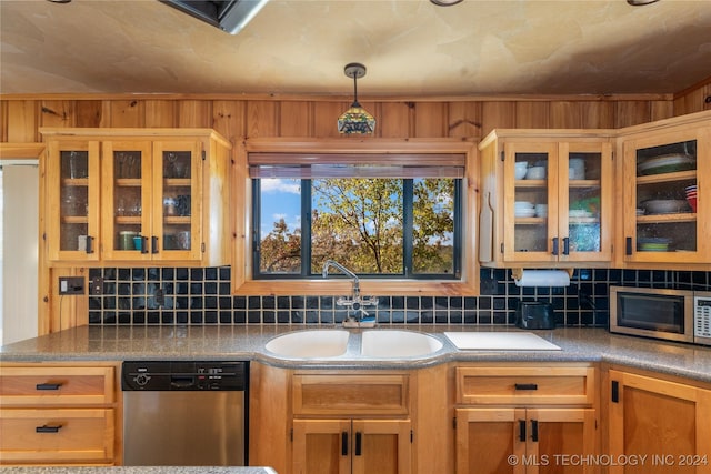 kitchen with wood walls, sink, stainless steel appliances, and decorative light fixtures