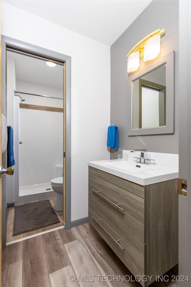 bathroom featuring toilet, vanity, wood-type flooring, and walk in shower