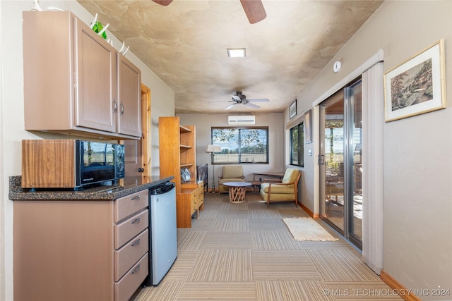 kitchen with an AC wall unit, ceiling fan, light brown cabinets, light colored carpet, and dark stone countertops