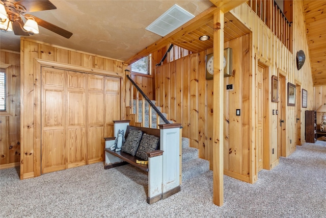 stairway featuring ceiling fan, wood walls, and carpet floors