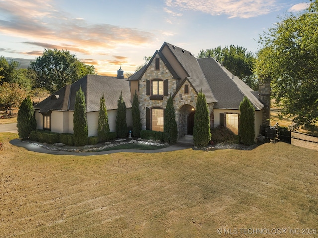 french provincial home with stone siding, a chimney, and a yard