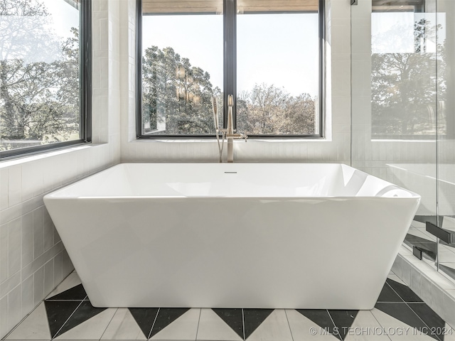 bathroom with a tub, tile patterned floors, plenty of natural light, and tile walls