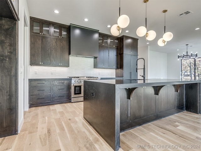 kitchen with gas stove, wall chimney range hood, light hardwood / wood-style flooring, pendant lighting, and dark brown cabinetry