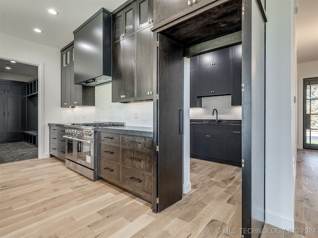 kitchen featuring range with two ovens, light hardwood / wood-style floors, wall chimney exhaust hood, dark brown cabinetry, and sink