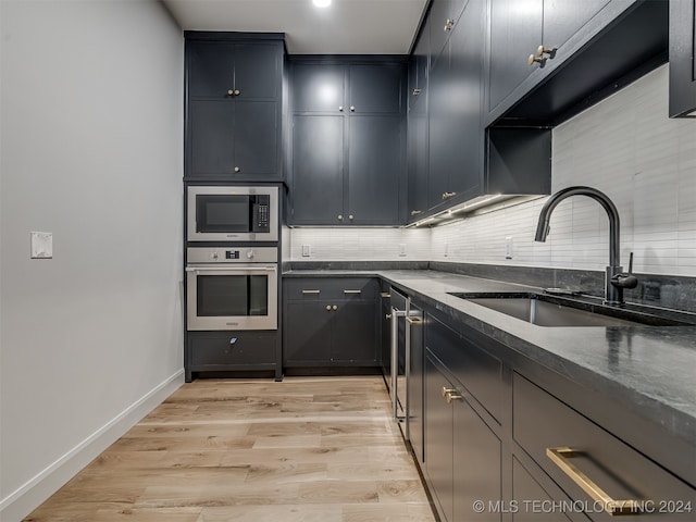 kitchen featuring stainless steel appliances, dark stone countertops, sink, light hardwood / wood-style floors, and tasteful backsplash