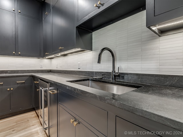 kitchen with sink, backsplash, light hardwood / wood-style floors, dark stone countertops, and wine cooler