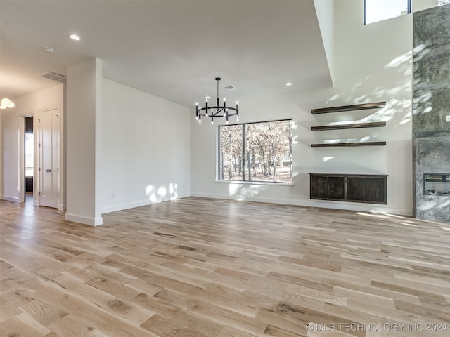 unfurnished living room with a large fireplace, light hardwood / wood-style flooring, and an inviting chandelier