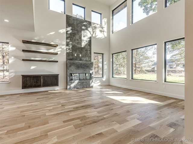 unfurnished living room featuring a large fireplace, a high ceiling, and light hardwood / wood-style floors