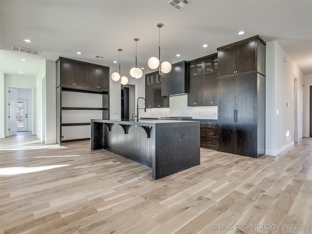 kitchen featuring custom range hood, light hardwood / wood-style floors, dark brown cabinetry, and a kitchen island with sink