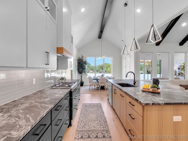 kitchen with a spacious island, light hardwood / wood-style flooring, dark stone countertops, sink, and decorative light fixtures