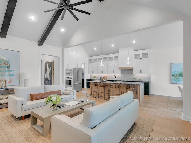 living room featuring beam ceiling, light hardwood / wood-style flooring, sink, high vaulted ceiling, and ceiling fan