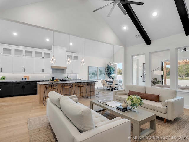 living room featuring sink, light hardwood / wood-style floors, ceiling fan, beamed ceiling, and high vaulted ceiling