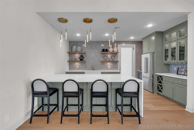 kitchen featuring decorative backsplash, high end fridge, light hardwood / wood-style flooring, green cabinetry, and pendant lighting