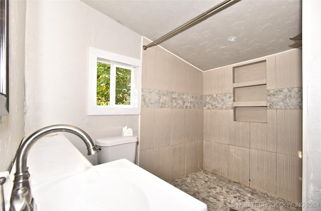 bathroom featuring a tile shower, sink, and toilet