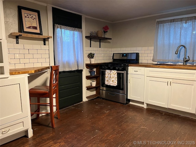 kitchen featuring butcher block counters, sink, stainless steel gas range oven, white cabinets, and backsplash