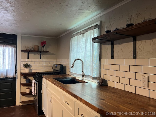 kitchen with butcher block countertops, sink, white cabinetry, a wealth of natural light, and stainless steel range oven