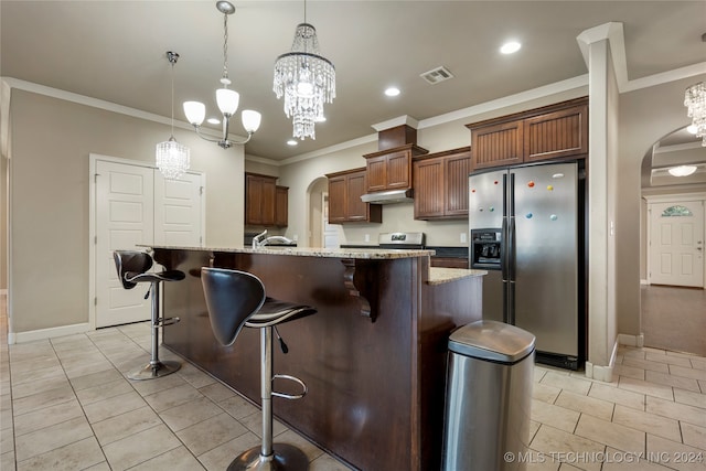 kitchen featuring a breakfast bar area, appliances with stainless steel finishes, decorative light fixtures, and a center island with sink