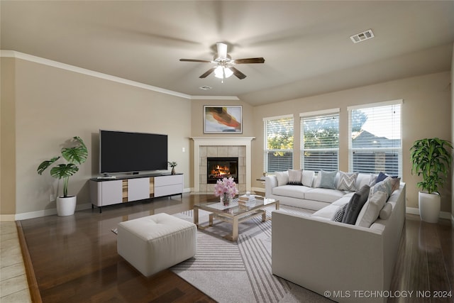 living room featuring crown molding, dark hardwood / wood-style floors, a tiled fireplace, and ceiling fan