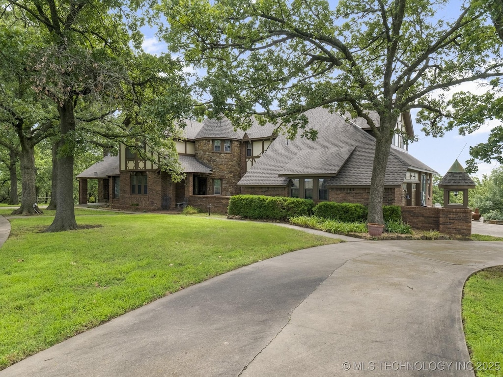 tudor home with brick siding, a shingled roof, and a front lawn