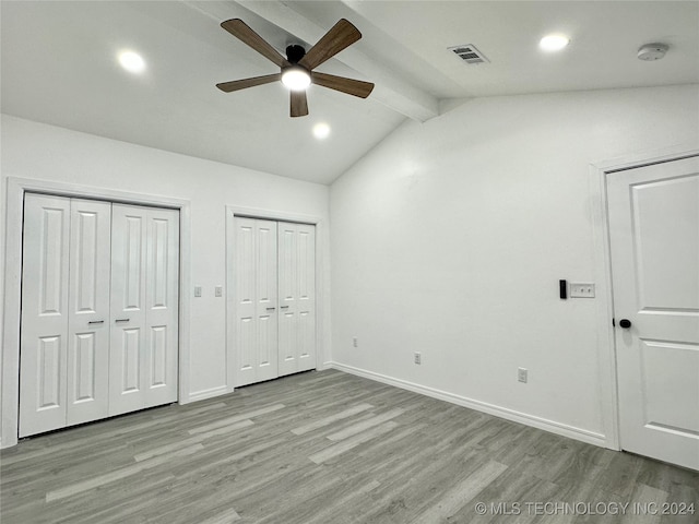 unfurnished bedroom featuring ceiling fan, lofted ceiling with beams, light wood-type flooring, and two closets