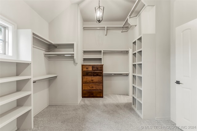 spacious closet with lofted ceiling, a notable chandelier, and light carpet