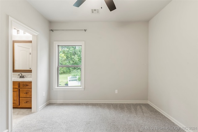 unfurnished bedroom featuring ensuite bathroom, light colored carpet, sink, and ceiling fan