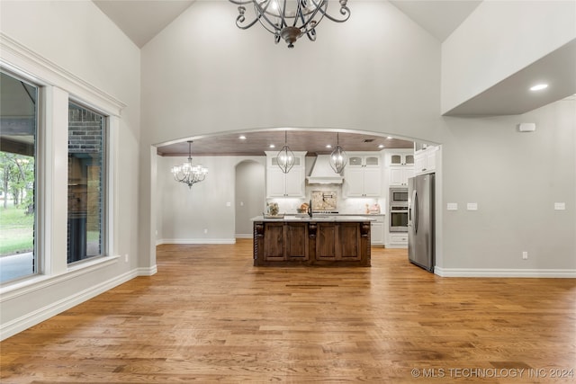 kitchen featuring custom exhaust hood, decorative light fixtures, a center island with sink, and wood-type flooring