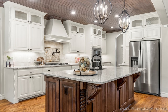 kitchen with stainless steel appliances, wood-type flooring, a center island with sink, custom exhaust hood, and white cabinetry