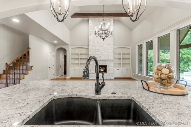 kitchen featuring sink, light wood-type flooring, a fireplace, decorative light fixtures, and light stone counters