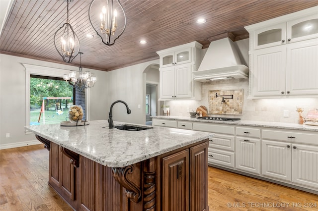 kitchen featuring a center island with sink, sink, white cabinets, light wood-type flooring, and premium range hood