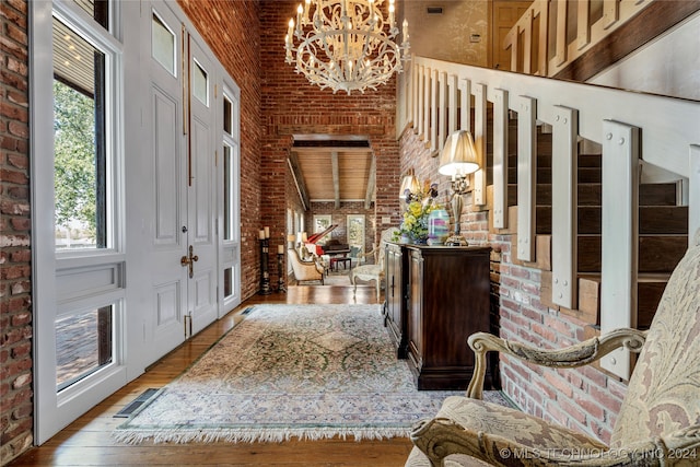 entryway with brick wall, a towering ceiling, and wood-type flooring