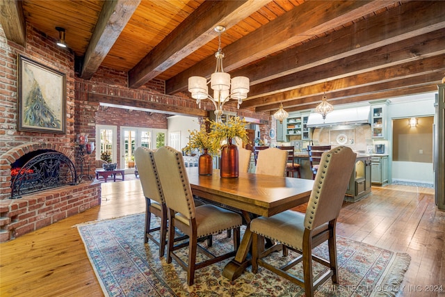 dining room featuring beam ceiling, light hardwood / wood-style flooring, a fireplace, and wooden ceiling