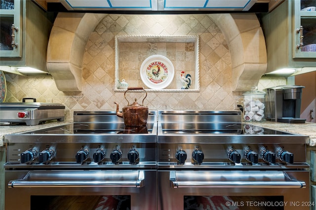 interior details featuring light stone counters, high end stainless steel range, and decorative backsplash