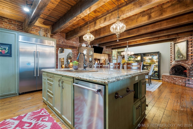 kitchen with beam ceiling, appliances with stainless steel finishes, a center island with sink, and hanging light fixtures