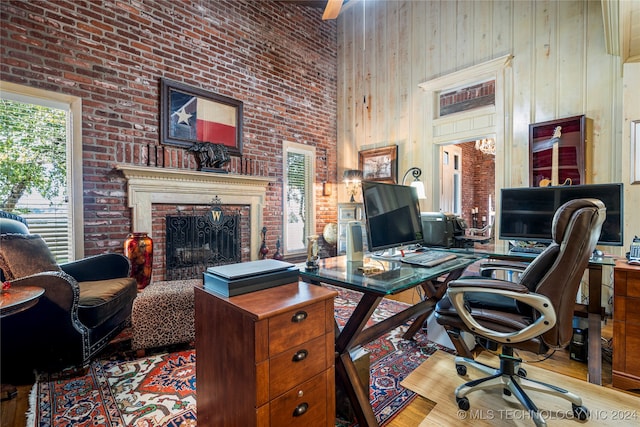 office area featuring a fireplace, a high ceiling, wooden walls, brick wall, and light hardwood / wood-style flooring