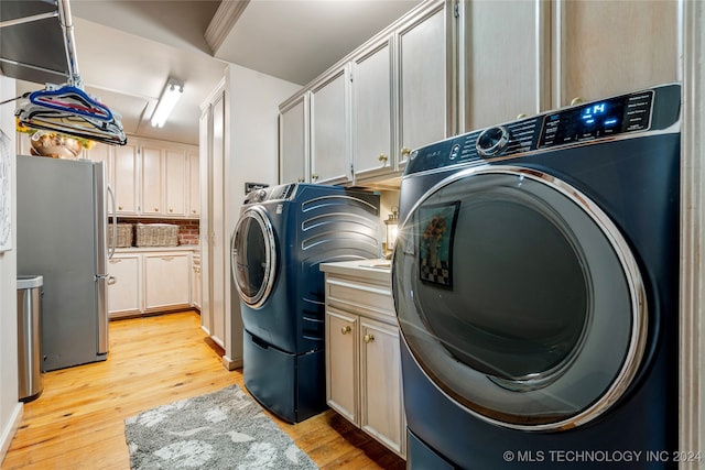 clothes washing area with light hardwood / wood-style flooring, washer and dryer, and cabinets