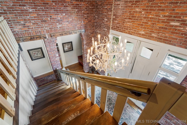 staircase featuring brick wall, a notable chandelier, and wood-type flooring