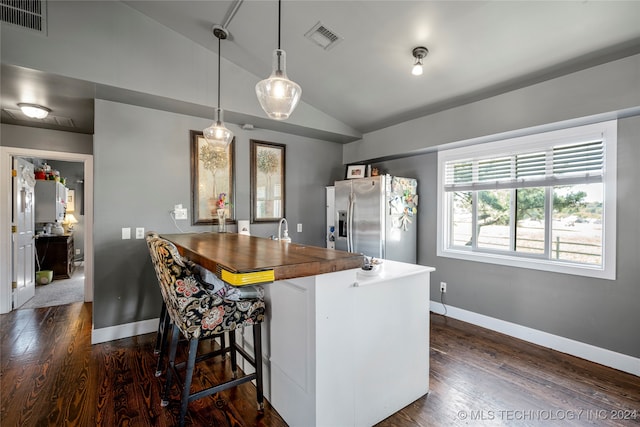 kitchen with dark hardwood / wood-style flooring, kitchen peninsula, a kitchen breakfast bar, stainless steel fridge, and lofted ceiling