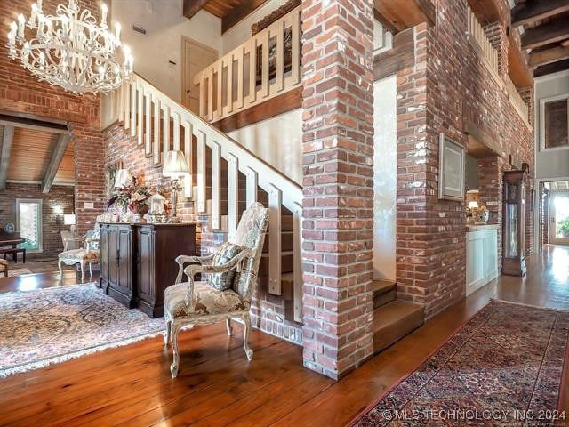 staircase with beam ceiling, wood-type flooring, brick wall, a notable chandelier, and a towering ceiling