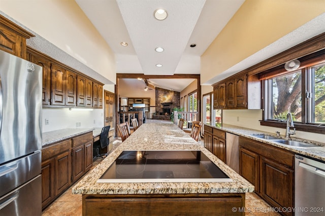 kitchen featuring a stone fireplace, sink, a kitchen island, and appliances with stainless steel finishes