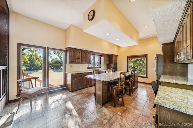 kitchen featuring a kitchen island, a kitchen bar, light stone countertops, and stainless steel refrigerator