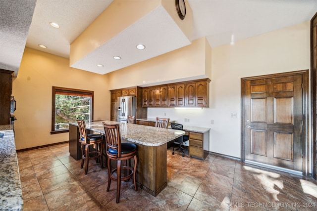 kitchen with light stone countertops, stainless steel fridge with ice dispenser, a textured ceiling, a breakfast bar area, and a kitchen island