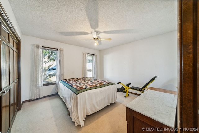 bedroom with ceiling fan, light carpet, and a textured ceiling