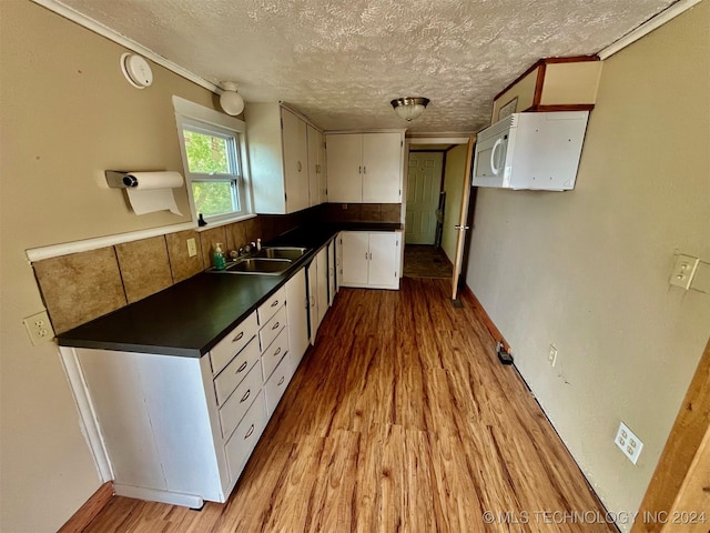 kitchen featuring white cabinets, dark countertops, a sink, light wood-type flooring, and a textured ceiling