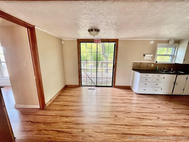 unfurnished dining area featuring light wood-style floors, a sink, baseboards, a textured ceiling, and crown molding