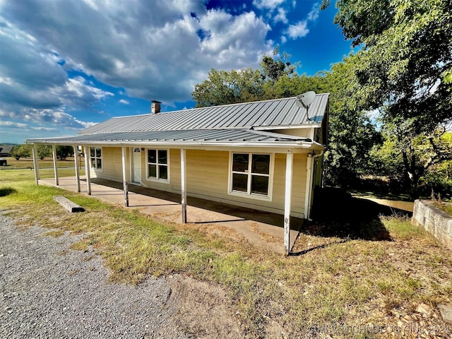 view of home's exterior featuring a patio, a standing seam roof, metal roof, a yard, and a chimney