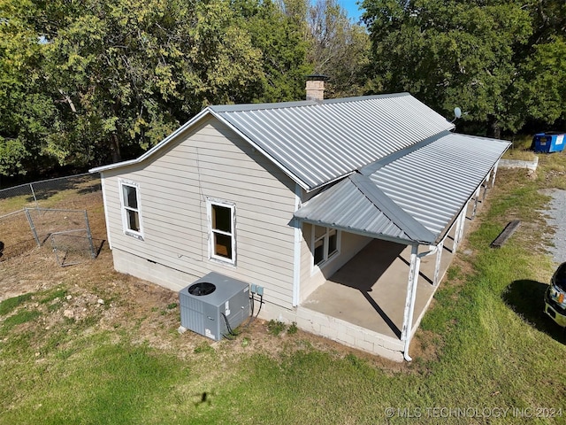 back of property with cooling unit, a patio, a chimney, metal roof, and fence