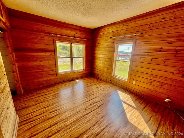 empty room featuring light hardwood / wood-style flooring, a textured ceiling, wooden walls, and plenty of natural light