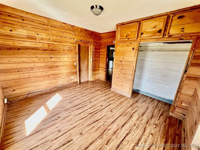 unfurnished bedroom featuring wood walls, a textured ceiling, and light wood-type flooring